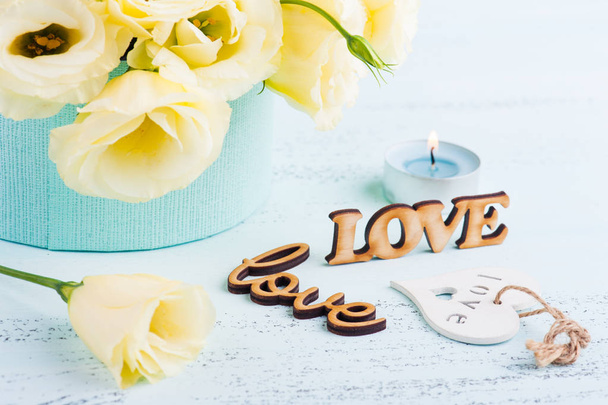 Eustoma κίτρινα λουλούδια, αναμμένο κερί μπλε, λέξη αγάπη στο τραπέζι. Ευχετήρια κάρτα γενεθλίων, Γυναικεία ή ημέρα της μητέρας - Φωτογραφία, εικόνα