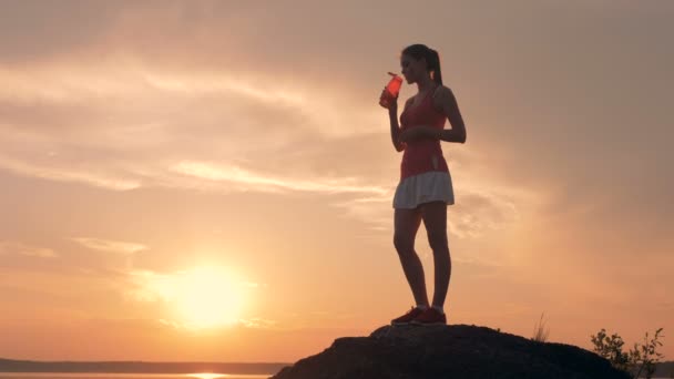 スポーツ フォームの若い女性は岩の上に立って飲んだり - 映像、動画