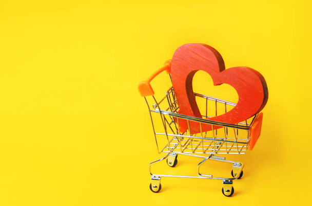 red heart in the supermarket trolley. concept of buying love. Valentine's Day. yellow background. Love of shopping. Favorite store. Buy love and happiness. Intimate services for money - Fotoğraf, Görsel
