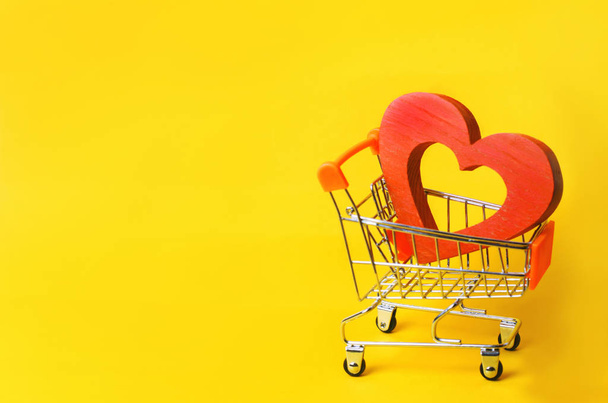 coração vermelho no carrinho do supermercado. conceito de comprar amor. Dia dos Namorados. fundo amarelo. Adoro fazer compras. Loja preferida. Compre amor e felicidade. Serviços íntimos por dinheiro
 - Foto, Imagem