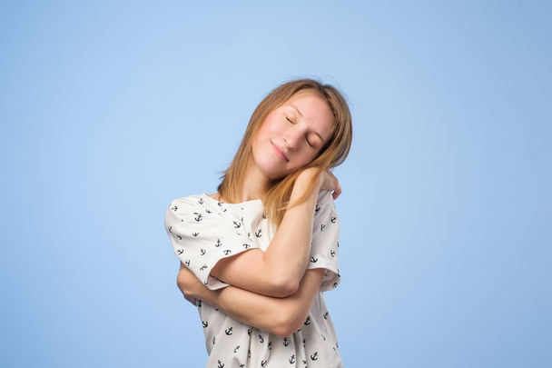Happy european woman hugging herself with natural emotional enjoying face on blue background. Love concept of yourself body - Photo, Image