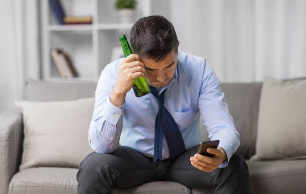 man with smartphone and bottle of beer at home - Foto, Imagen