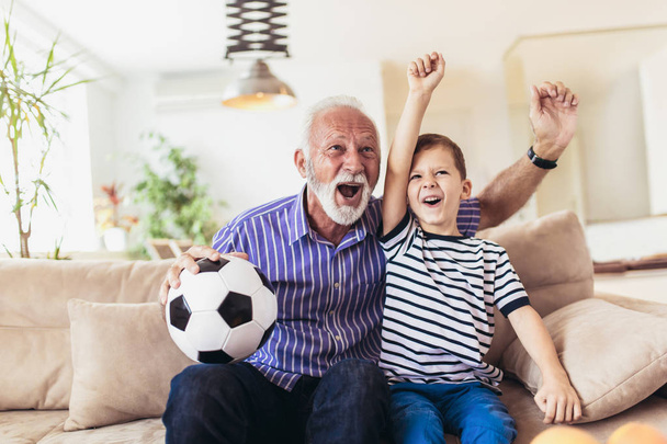 Little boy on couch with grandfather cheering for football game  - Foto, Bild