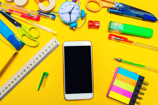 Creative school desk with accessories. stationery. Phone with an isolated screen. copy space. the concept of school and education. colored pens, pencils, stickers, notepad. yellow background, top view - Photo, Image