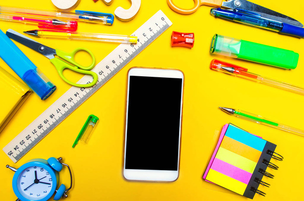 Creative school desk with accessories. stationery. Phone with an isolated screen. copy space. the concept of school and education. colored pens, pencils, stickers, notepad. yellow background, top view - Photo, image