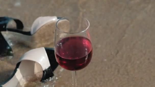 shoes lie on the seashore, a glass of wine lies beside - Imágenes, Vídeo