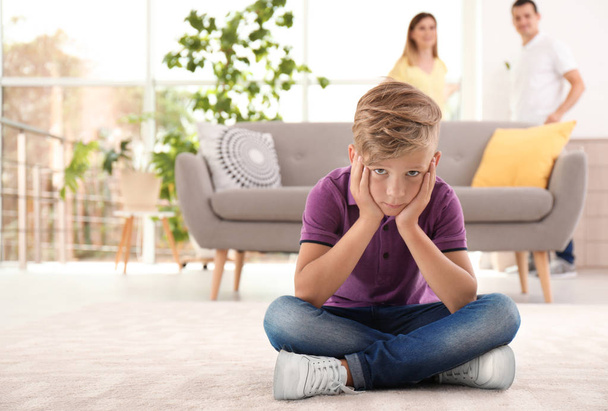 Upset child sitting on floor while parents fighting on background. Family relationships - Foto, Bild