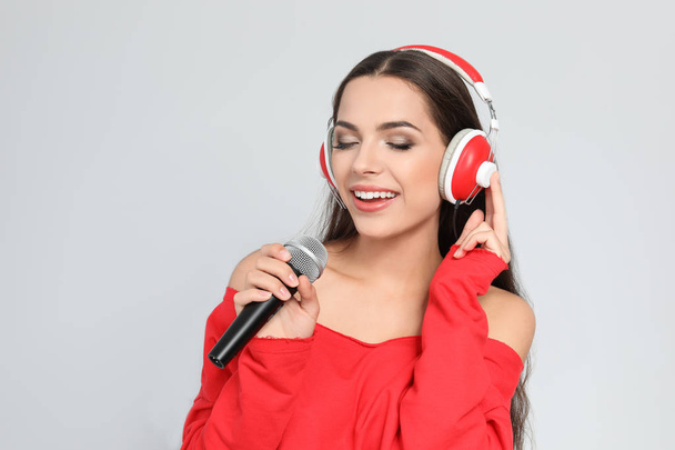 Young woman singing into microphone on color background. Christmas music - Fotó, kép