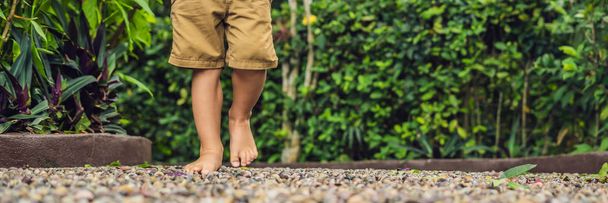 Boy Walking On A Textured Cobble Pavement, Reflexology. Pebble stones on the pavement for foot reflexology. BANNER long format - 写真・画像