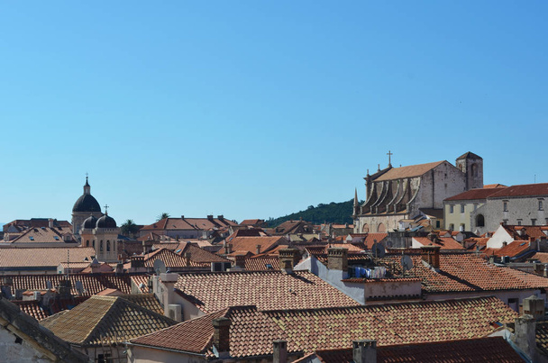 A view over the terracotta tiles covering the roofs of Dubrovnik. Some washing can be seen. The cathedral is to one side. The sky is blue. - 写真・画像
