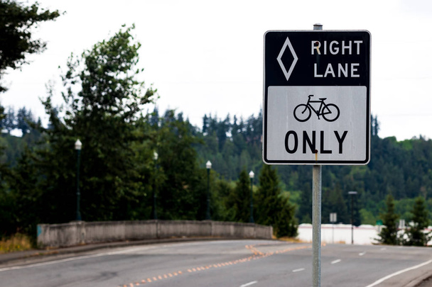 Right lane bikes only black and white sign with road and tree - Photo, Image