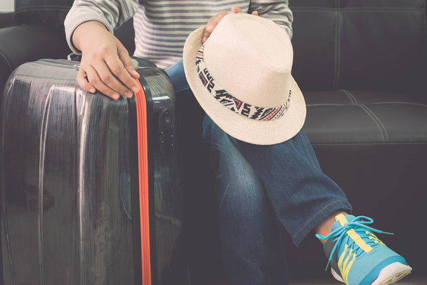 女性旅行者は旅行バッグと麦わら帽子空港で革のソファで座っています。旅行の概念. - 写真・画像