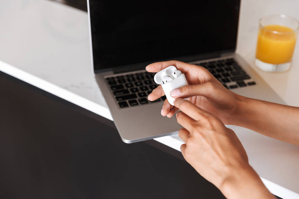 Close up of woman holding earphones in white case with laptop computer on a background - Fotó, kép