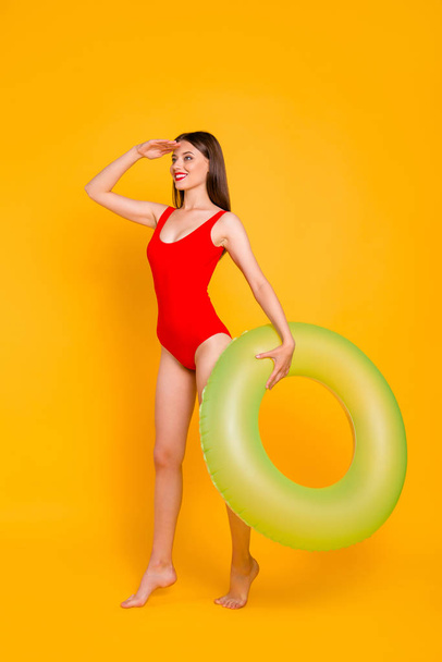 Where is my vacation? Full-legh vertical portrait of excited girl in a colorful swimsuit holds inflatable lifebuoy and looks forward isolated on vivid yellow background - Foto, Bild