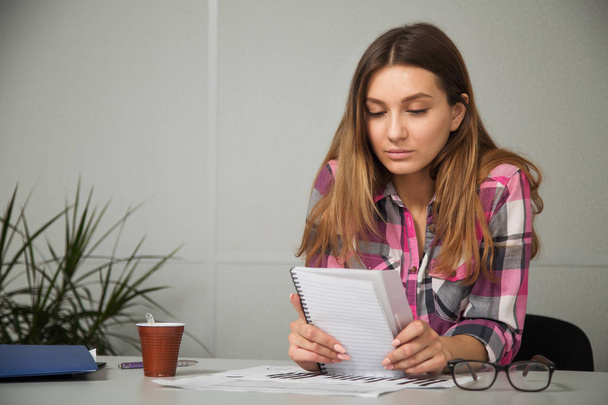young businesswoman girl with glasses in casual wear sitting at the table carefully look at the documents  - Photo, image
