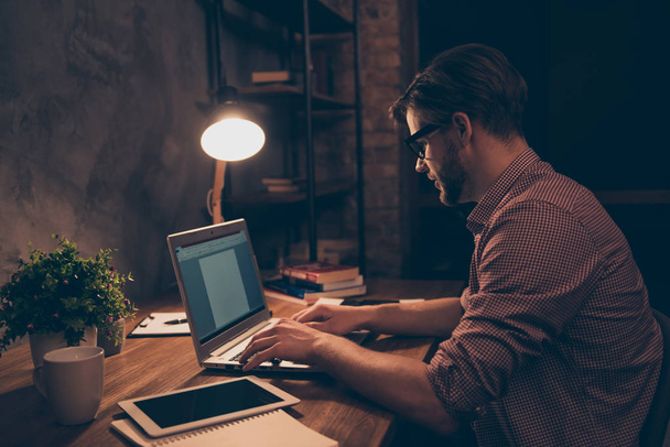 Side view portrait of attractive, hard worker, busy man in shirt with hairstyle, stubble working at night, taking work at home, sitting in workplace, workstation holding hands on keypad - Foto, immagini