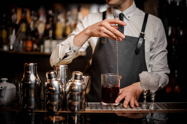 Bartender stirring a fresh and tasty summer alcoholic cocktail in glass on the bar counter - Фото, зображення