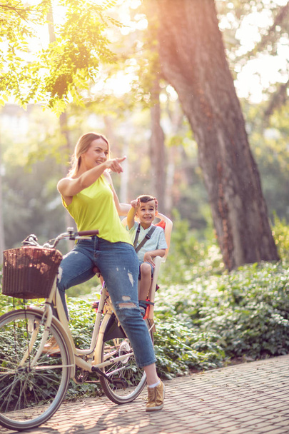 Family sport and healthy lifestyle -Happy mother and son riding a bicycle together outdoors in a city park - 写真・画像