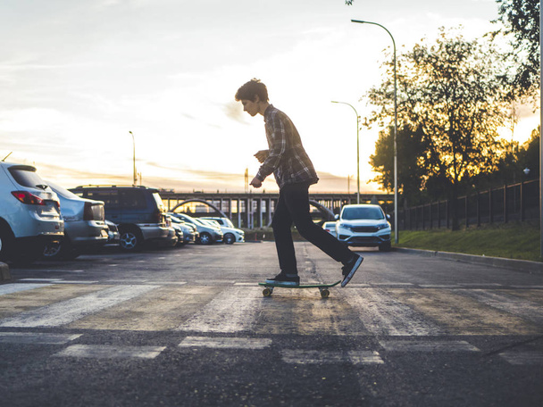 silhouet van stijlvolle man in casual outfit de penny skateboard rijden op de oversteekplaats stad - Foto, afbeelding