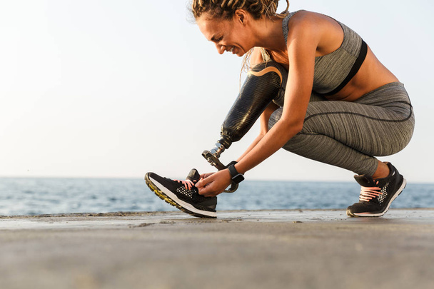 Smiling disabled athlete woman with prosthetic leg tying shoelace outdoor - Φωτογραφία, εικόνα