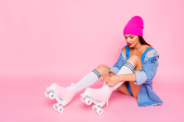 Attractive girl in stockings on roller skates ties up the shoelaces isolated on bright pink background - Foto, Imagem