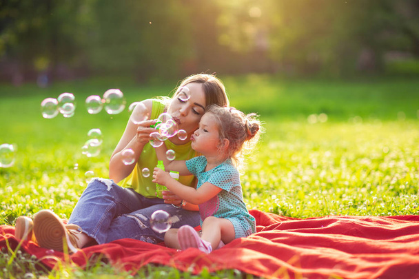 Family in park -Cute female child blows soup foam and make bubbles with her mother in nature - Φωτογραφία, εικόνα