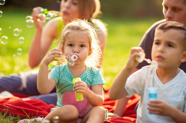 Familie im Park - süßes kleines Mädchen pustet Seifenblasen - Foto, Bild