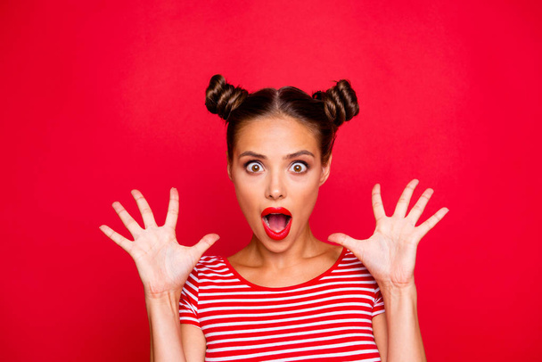 Closeup portrait of shocked girl with brown eyes and red lipstick on the mouse look at the camera with his fingers spread wide. Concept of advertising isolated on red background - Photo, image