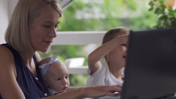 Woman with children works on laptop in cafe - Materiał filmowy, wideo