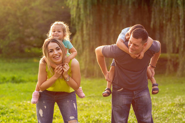 Rodzina piggyback ich dzieci i wspólną zabawę w parku - Zdjęcie, obraz