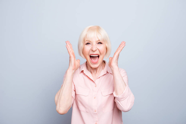 Old adult blonde glad excited cheerful astonished lady smiling, laughing, screaming, raising hands to cheeks, opened mouth, over grey background, isolated - Foto, Imagem