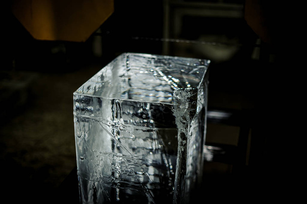 Big clear ice cube standing on the floor on the ice production plant under the light equipment on the blurred background - Foto, immagini