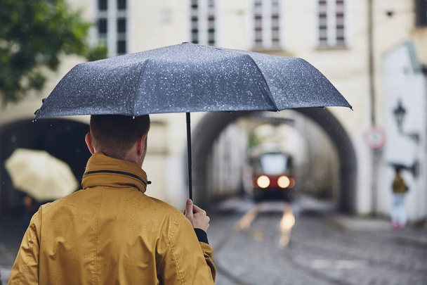 Young man holding umbrella walking in rain. Old city street in Prague, Czech Republic  - Photo, Image