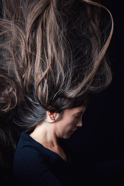 Girl throwing hair in the air on black background. Concept image for bad hair day - Foto, Imagem