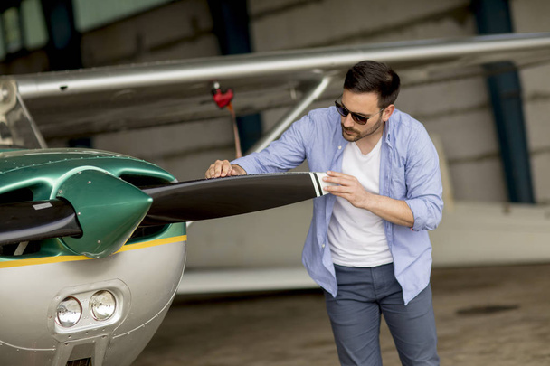 Handsome young pilot checking his ultralight airplane in the hangar before flight - Photo, Image