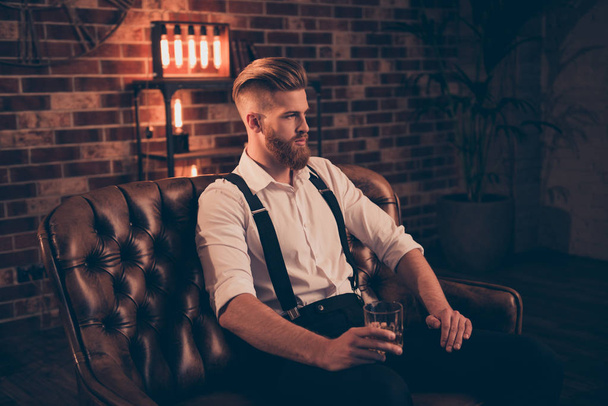 Portrait of stunning serious confident handsome thinking pondering pensive focused concentrated relaxed dreamy planning entrepreneur sitting on leather divan enjoying alcohol beverage in hands - Zdjęcie, obraz