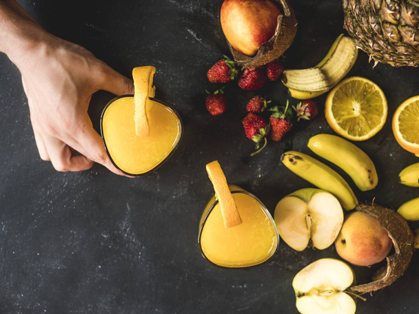mão tomando o smoothie laranja fresco na mesa preta com frutas frescas de verão
 - Foto, Imagem