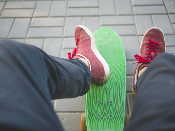 κλείνω τα πόδια του ανθρώπου σε πάνινα παπούτσια κάθονται στον πάγκο με skateboard - Φωτογραφία, εικόνα