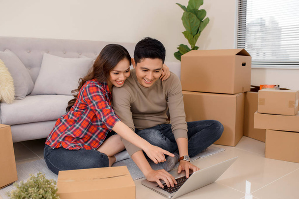 Fiatal házaspár egy új otthon. Férfi és nő, notebook laptop számítógép és dobozok. - Fotó, kép