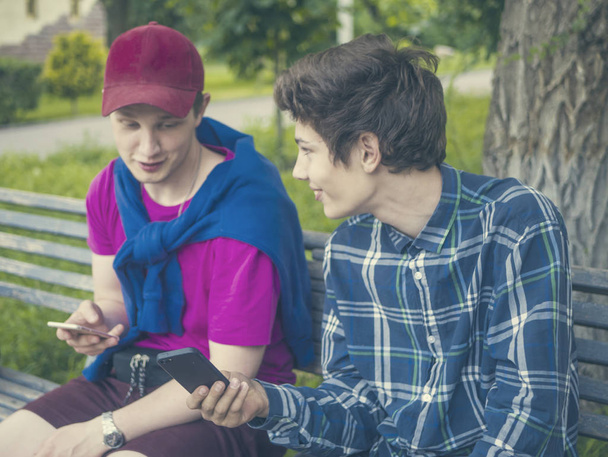 δύο νεαρά αδέλφια σε casual κάθονται στον πάγκο και να συνομιλείτε με τους vintage smarphone τονισμένα - Φωτογραφία, εικόνα