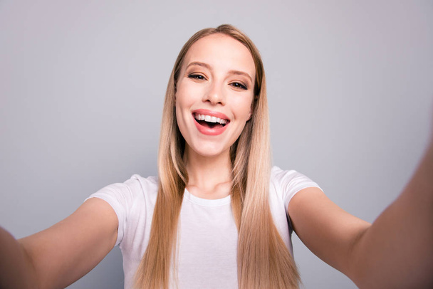 Close up portrait of attractive cute cheerful blond lady taking selfie on front camera of smartphone isolated on gray background - Фото, изображение