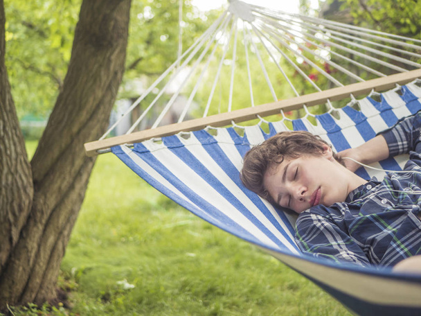 nuori mies teini nukkuu riippumatossa puutarhassa kesäpäivänä
 - Valokuva, kuva