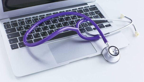 Stethoskop liegt auf einer Laptop-Tastatur in einem Konzept der Online-Medizin oder die Fehlerbehebung des Computers betrachtet niedrigen Winkel mit Kopierraum. - Foto, Bild