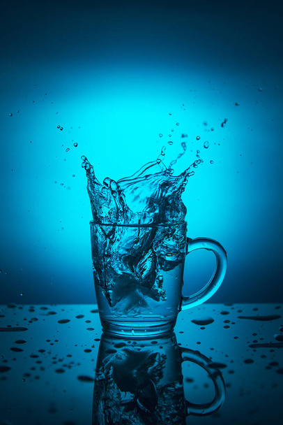 青い背景上のカップの水のしぶき. - 写真・画像