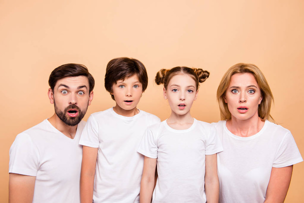 Closeup portrait of young family, bearded father, blonde mother and their little children, boy and girl, wearing white T-shirts showing surprising on camera on beige background - Zdjęcie, obraz