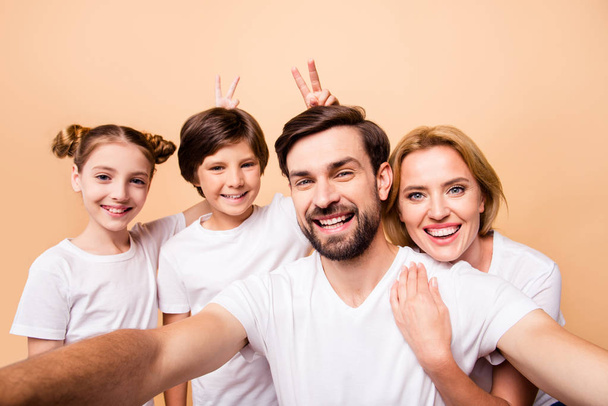 Young adorable attractive beautiful happy family laughing making selfie together. Boy and girl holding victory or peace sign behind their relatives' heads, mimicking bunny ears - Photo, image