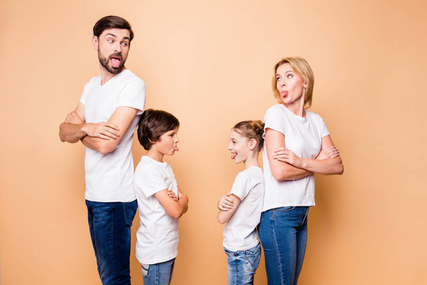Portrait of attractive beautiful family, bearded father, blonde mother standing back to back with their little children wearing jeans and white T-shirts, with crossed arms. Showing each other tongues - Фото, зображення
