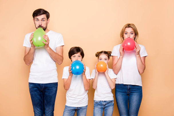 Young family, bearded father, blonde mother, boy and girl wearing blue jeans and white T-shirts, blowing air balls green beige red blue - 写真・画像