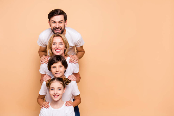 Young smiling family, bearded father, blonde mother, boy and girl wearing white T-shirts, standing in odrer of hierarchy, holding hands on each other's shoulders. Copy space - Foto, Bild