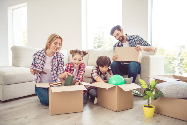 Young happy smiling family four persons unwrapping carton boxes with stuff in light living room, moving to new flat, renovation - Zdjęcie, obraz